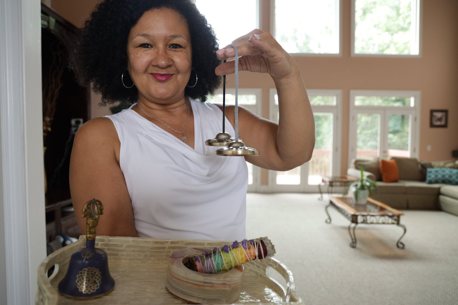 Linda K. Harmony holding a tray of space clearing tools including tingsha cymbals used during energetic space clearing ceremonies.