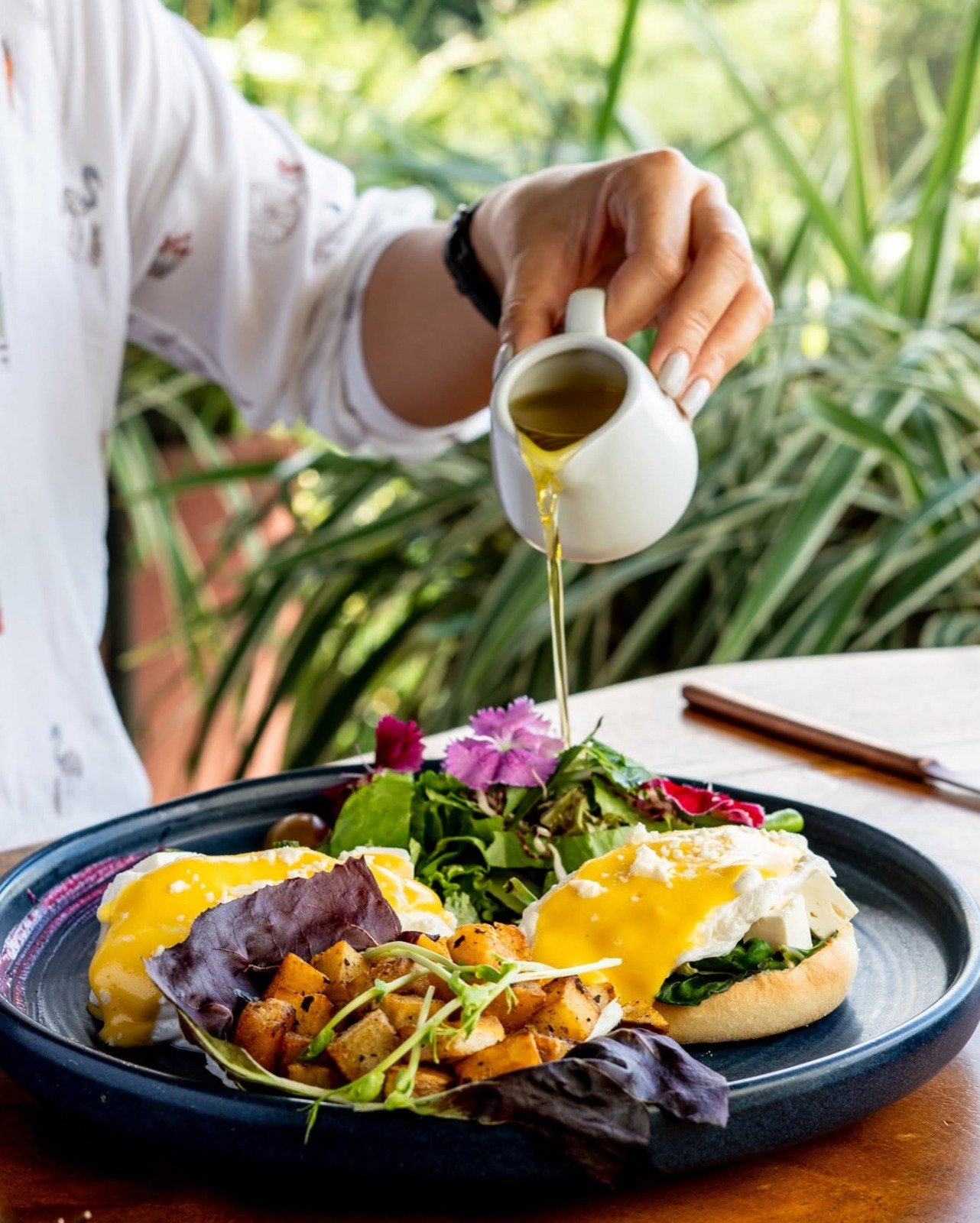 Pouring Hollandaise Sauce Over Eggs Benedict with Garden Views – Emilios Cafe Manuel Antonio Costa Rica
